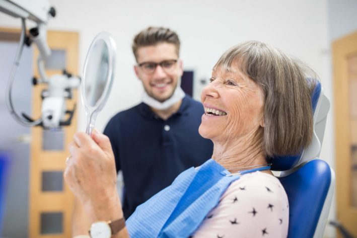 elderly woman smiling into mirror at dentist